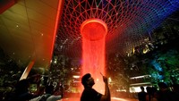 Orang-orang menonton layar cahaya di Rain Vortex setinggi 40 meter, yang merupakan air terjun indoor tertinggi di dunia, terlihat dari dalam Bandara Jewel Changi di Singapura. Orang-orang menonton layar cahaya di Rain Vortex setinggi 40 meter, yang merupakan air terjun indoor tertinggi di dunia, terlihat dari dalam Bandara Jewel Changi di Singapura.