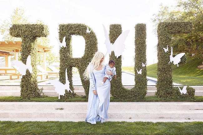 Selain balon, pesta ultah True juga dihiasi dekorasi bertema kupu-kupu. Mereka pun memakai baju kembaran berwarna biru pastel dan berpose di depan hiasan semak bertulisan TRUE, dengan banyak kupu-kupu putih di sekitarnya. Foto: Instagram/@khloekardashian