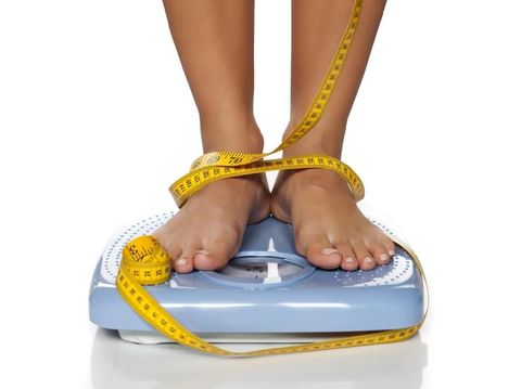 woman's feet on a domestic weight scale and measuring tape around them