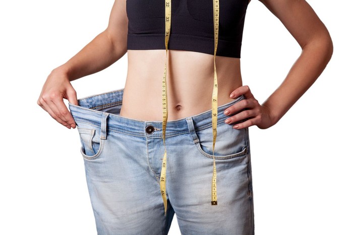 diet Close-up of slim waist of young woman in big jeans showing successful weight loss, isolated on white background, diet concept.