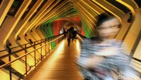 Warga melintas di JPO GBK yang kini berubah warna.