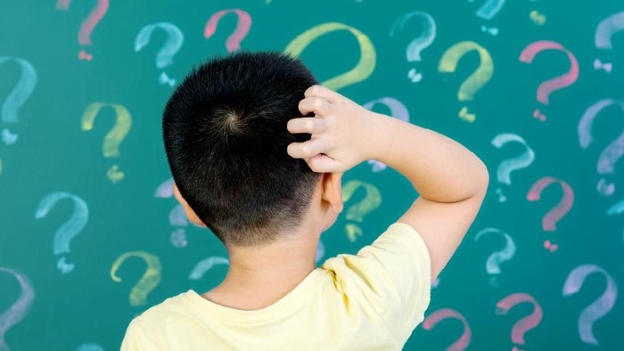 Asian boy in front of blackboard with question marks.