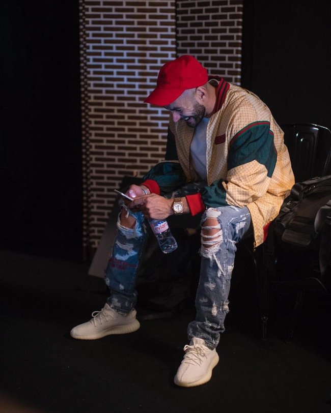 Memegang sebotol air mineral merek Evian, Karim Benzema tampil stylish memakai topi Balenciaga, jaket dari Gucci, jeans Off White dan sneakers Adidas Yeezy. Gayanya semakin mewah dengan jam tangan Audemars Piguet yang menghiasi pergelangan tangannya. (Foto: Instagram)