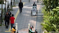Seorang pedagang mendorong gerobak dagangan melintasi trotoar di Jalan Sudirman, Jakarta, Selasa (23/4/2019).