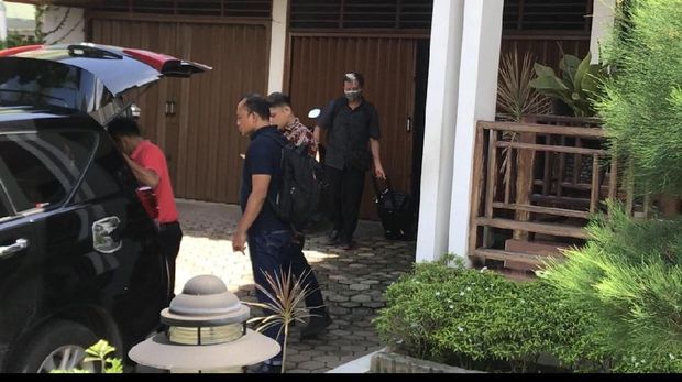 Seorang petugas membawa keluar koper berwarna hitam dari dalam rumah Muzni.