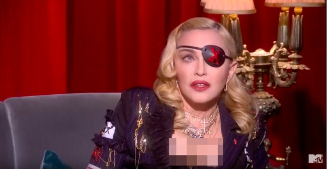 Menjadi bintang tamu acara bincang-bincang di MTV UK baru-baru ini, Madonna pun melengkapi gaya busananya dengan penutup mata itu. Ia tampil seksi dengan blazer berbelahan dada rendah yang dihiasi aksesori bernuansa emas. Foto: YouTube/MTV