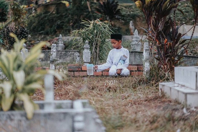 Mengenakan pakaian koko lengkap dengan peci sambil membawa teko air dan buku yasin, raut wajah bocah laki-laki ini terlihat sendu. Foto: Facebook Atan Mukris
