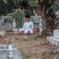 Mengenakan pakaian koko lengkap dengan peci sambil membawa teko air dan buku yasin, raut wajah bocah laki-laki ini terlihat sendu. Foto: Facebook Atan Mukris