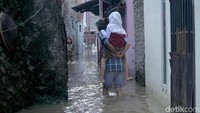 Seorang warga menggendong anaknya menuju ke lokasi yang lebih aman usai air merendam rumahnya.