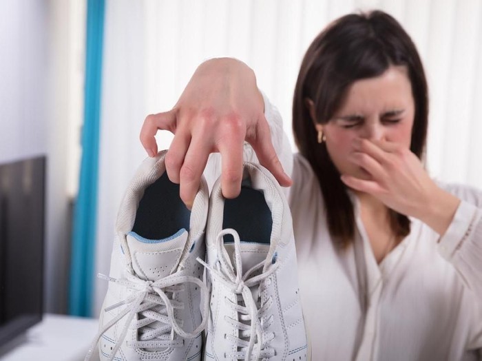 Ilustrasi sepatu bau Woman Holding Dirty Stinky Shoes Covering Her Nose