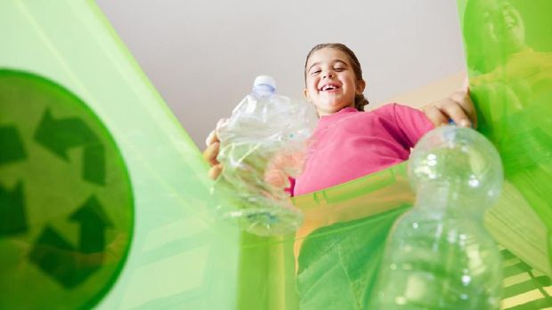 Girl holding plastic bottles for recycling, viewed from inside recycling bin. Copy space