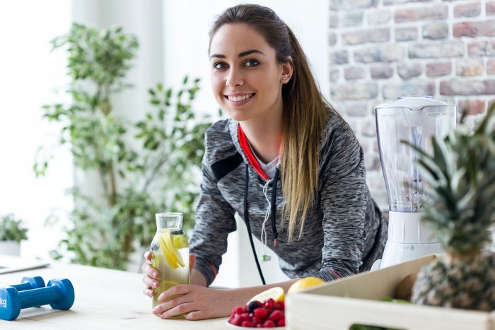 Shot of sporty young woman looking at camera while drinking lemon juice in the kitchen at home.