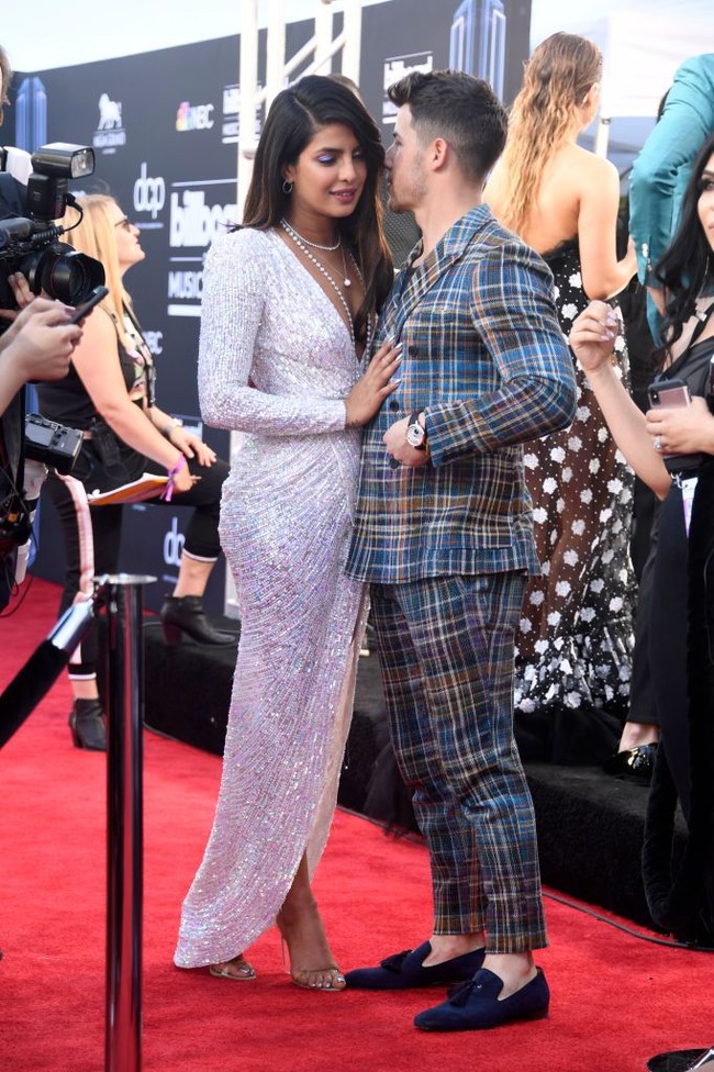 Pada ajang Billboard Music Awards 2019, Nick Jonas tampil bersama dua saudaranya Joe Jonas dan Kevin Jonas membawakan single terbaru dari band mereka Jonas Brothers, Sucker. Dan saat tampil itu mendadak Nick memberikan kejutan manis pada Priyanka Chopra. Penyanyi tampan itu mencuri-curi kesempatan mencium aktris India tersebut. Sambil berjalan ke atas panggung dan bermain gitar, Nick mendaratkan ciuman pada Priyanka. Foto: Dok. Getty Images, Instagram