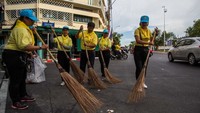 Sejumlah relawan mengenakan pakaian berwarna kuning nampak membersihkan jalan di sekitar area Istana Kerajaan Thailand jelang penobatan Raja Maha Vajiralongkorn.