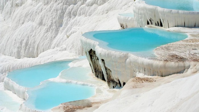 Illuminated Pamukkale terraces against sunset sky background. Denizli city lights in the middle of composition.