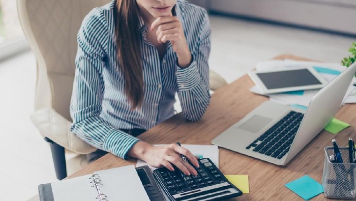 Close up cropped photo of strict young business woman accountant in formal wear and with pony tale, sitting at her work place and counting profit