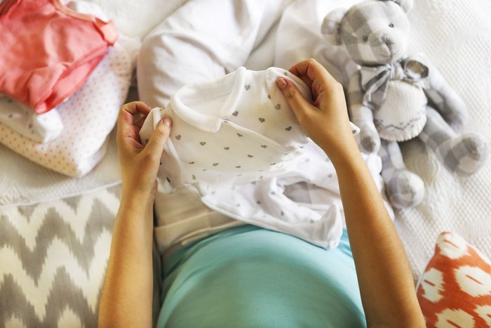 Pregnant woman is packing baby clothes for going to maternity hospital top view