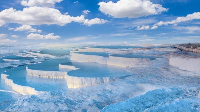 Illuminated Pamukkale terraces against sunset sky background. Denizli city lights in the middle of composition.