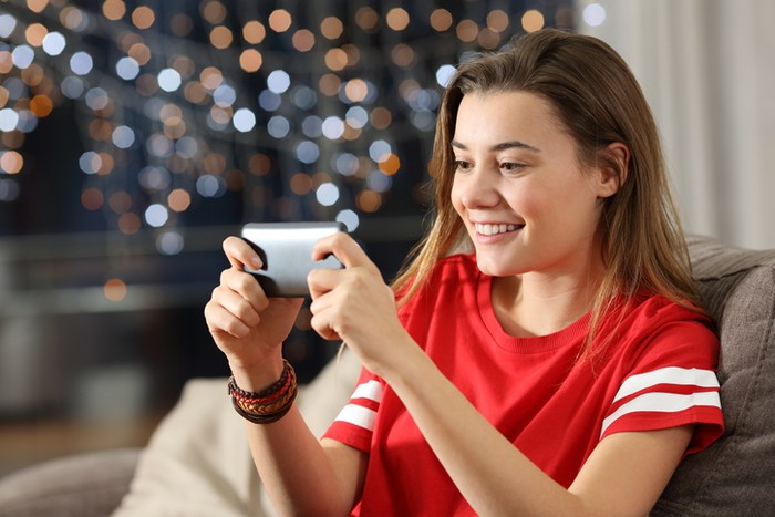 Teen watching media in a smart phone in the night sitting on a couch in the living room at home