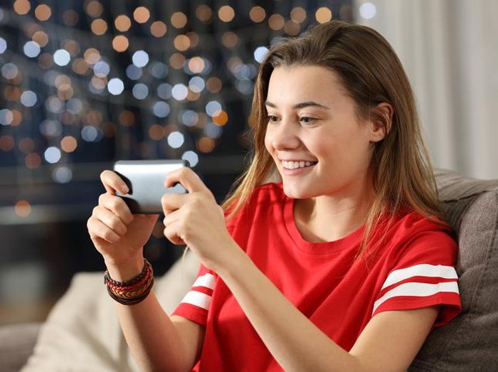 Teen watching media in a smart phone in the night sitting on a couch in the living room at home