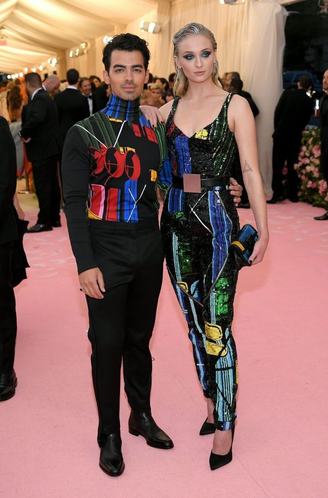 Sophie menebar pesonanya dengan jumpsuit edgy penuh warna dari Louis Vuitton. Joe pun tampil serasi dengan turtleneck berwarna senada. (Foto: Getty Images)