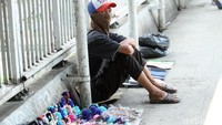 Seorang pedagang tampak menunggu pembeli dengan duduk di samping dagangannya.