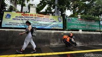 Warga berjalan di depan spanduk larangan berjualan di trotoar.