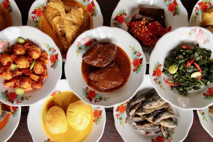Assortment of Minangkabau dishes served on the table in hidang style; means serving the eaterys menu on the table. The dishes are plated on small ceramic plates and stacked as to save some spaces on the table.