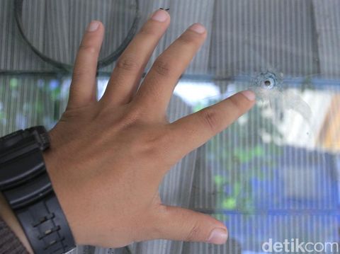 Warga memperlihatkan kaca rumahnya yang bolong ditembus peluru.