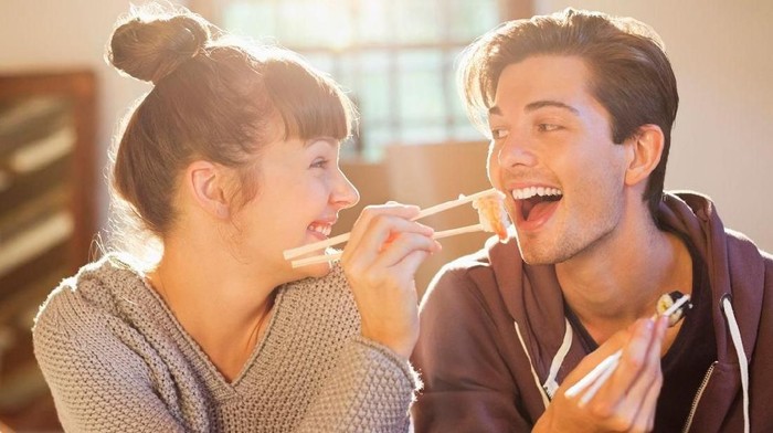 Affectionate couple sitting in the outdoor restaurant in the evening, beautiful blonde woman eating tomato soup.