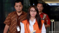 Sri Wahyumi nampak mengenakan kemeja putih yang dilapisi dengan rompi oranye KPK. Ia juga nampak mengenakan hak tinggi dan kacamata.