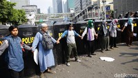 Sejumlah peserta aksi bergandengan tangan di depan barikade polisi bertameng.