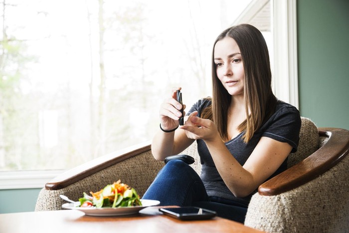 diabetes A young diabetic woman checking her blood sugar levels at home. A suitably healthy meal is infant of her on the table.