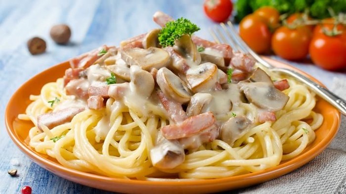 Spaghetti with Bechamel sauce, mushrooms and bacon on a wooden table