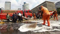 Anies tampak menyiram jalan protokol tersebut menggunakan selang dari damkar.