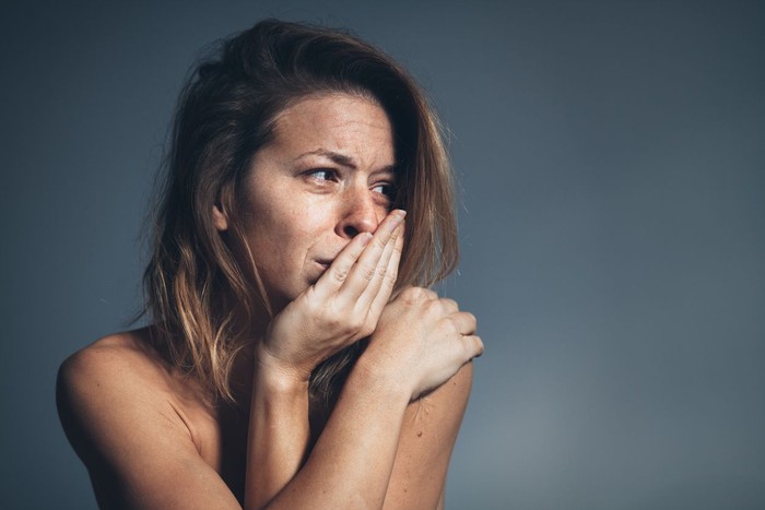 ilustrasi kekerasan dalam rumah tangga Young woman is sitting hunched at a table at home, the focus is on a mans fist in the foregound of the image