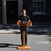 Momen pidato pengunduran diri Perdana Menteri Inggris Theresa May beberapa waktu lalu membuat seorang pria mendadak viral. Dia bukan pengganti Theresa, melainkan seorang teknisi audio yang mempersiapkan podium untuk Theresa berpidato di depan rumah dinas PM Inggris di 10 Downing Street, London. (Foto: Leon Neal/Getty Images)