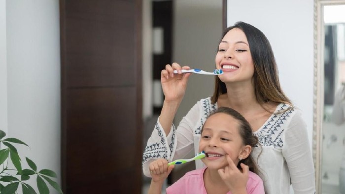 Children are brushing their teeth in the bathroom at home. The mother is checking the little boys mouth to make sure he has brushed properly.