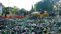 Alat berat menggilas ribuan botol miras berbagai merek.