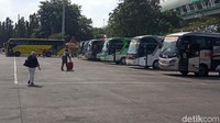 Membawa koper beberapa pemudik berjalan ke arah busnya yang mau berangkat.