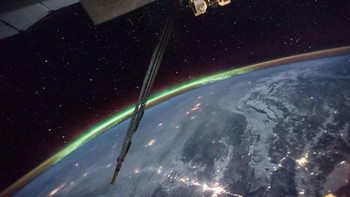 Foto long exposure dari ISS memperlihatkan Bumi diselimuti aurora di salah satu sisinya, cahaya dari perkotaan dan bintang-bintang jadi latar belakang. Foto: NASA
