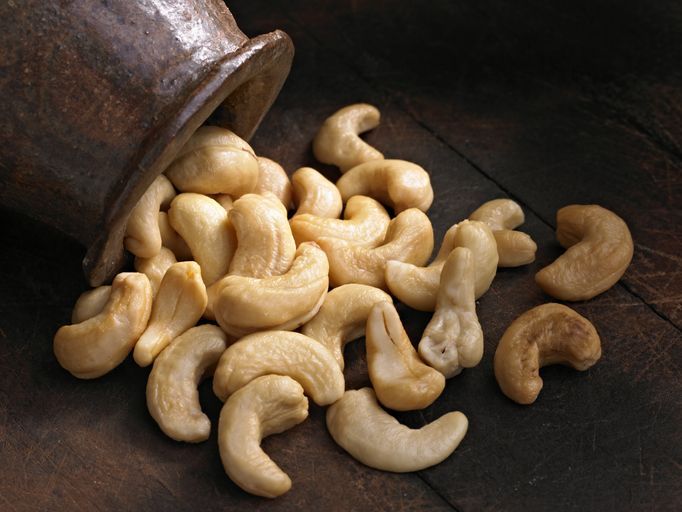 Wooden bowl of cashew nuts from above. On dark wood.