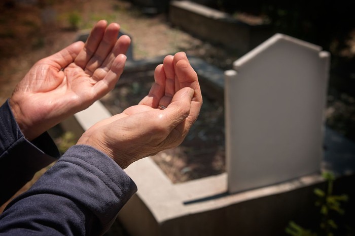 elderly muslim woman hands praying near the grave