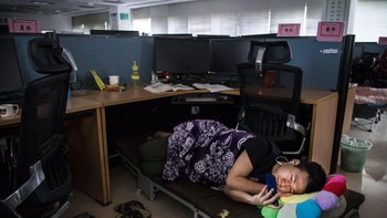 Seorang pegawai Huawei menatap smartphonenya sambil tiduran di kubikel, di kantor Huawei di Shenzen. Foto: Getty Images