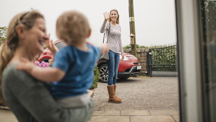 A women waves goodbye to her mother and son from across the street as she leaves the house.