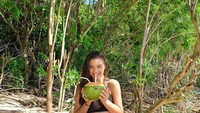 Sluuurp! Sebuah kelapa muda tengah dinikmati Angela. Wanita yang juga hobi traveling ke pantai ini melempar senyum manis sambil berpose. Foto: instagram @angelagilsha