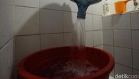 Seorang penghuni apartemen menuangkan air galon ke dalam bak mandi.