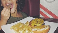 Nyam! Makan burger dengan isian patty dan keju mozarella. Noah tampak lahap sekali makannya. Foto: Instagram@ashrafsinclair