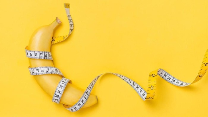 Diet, fitness and health concept presented by yellow banana wrapped in measure tape isolated on yellow paper background