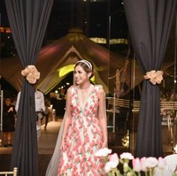 Gaun V-neck dengan latar warna putih tersebut dihiasi aplikasi tiga dimensi berbentuk bunga di seluruh bagiannya. Tampak pula train putih di bagian belakang sebagai aksen yang menambah kesan mewah. Foto: Instagram/@inijedar